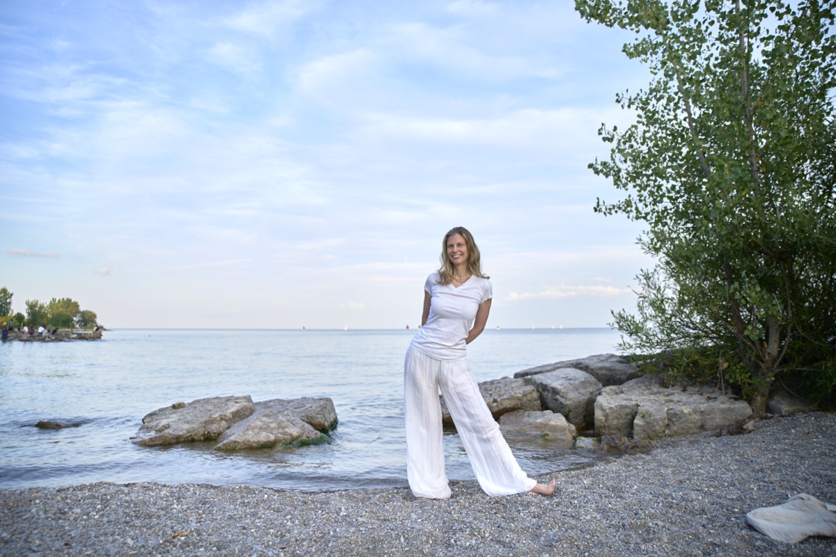 Julia Arbuckle seated on the Lake Ontario shoreline, smiling toward the camera.